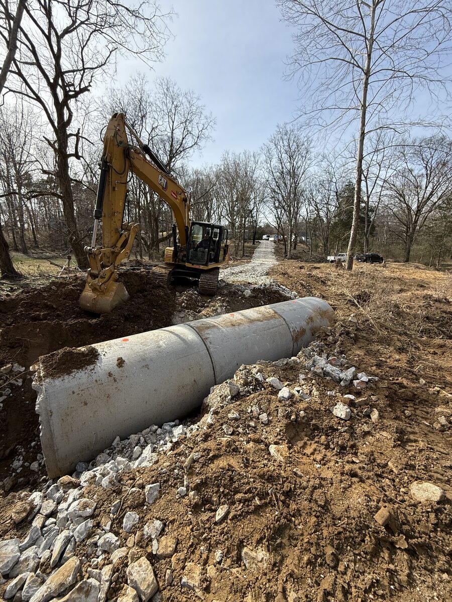 CAT excavator installing large concrete culvert pipe