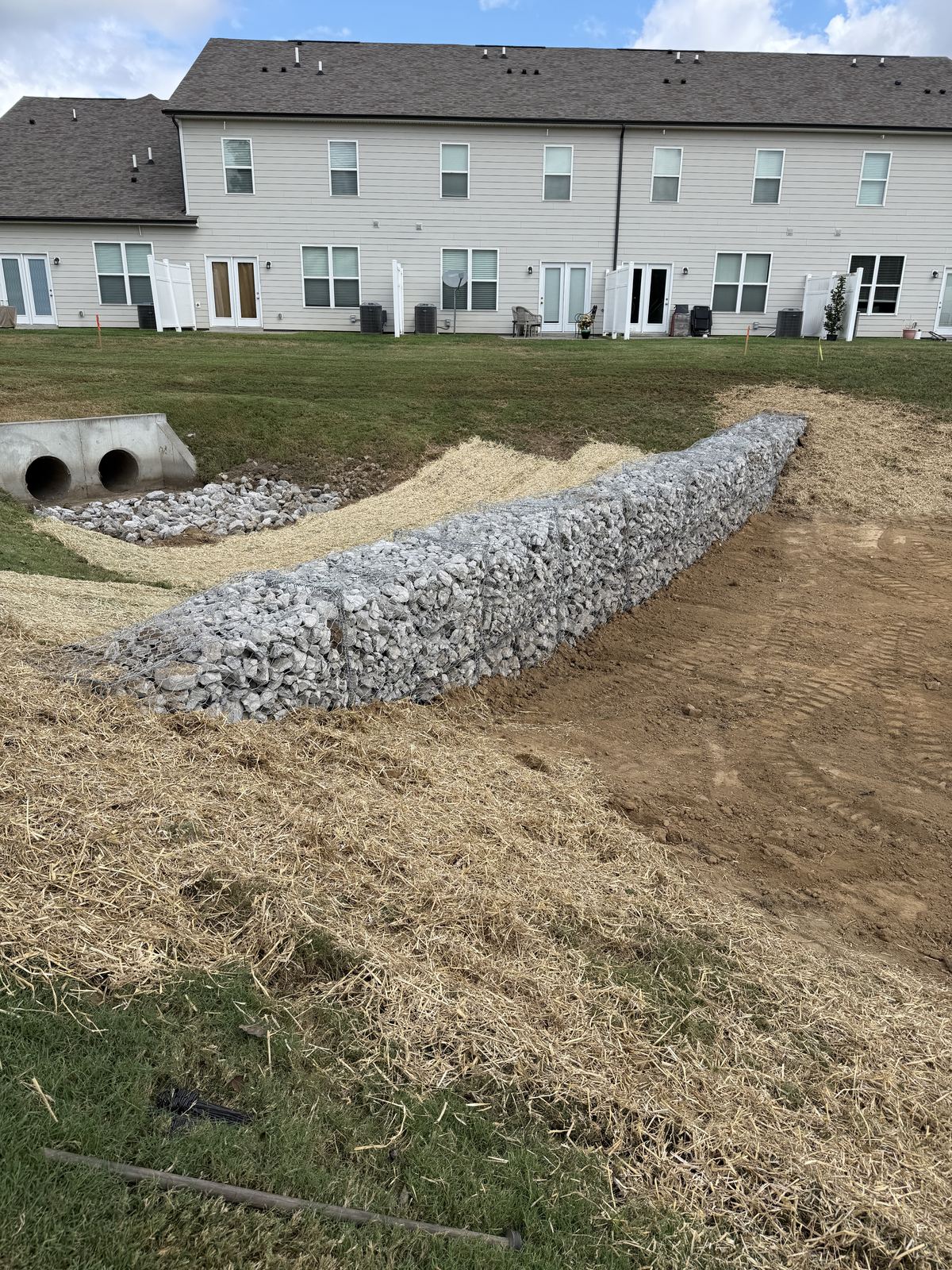 Stone-filled gabion basket wall across a stormwater pond forebay with rip rap and straw &mdash; Lebanon TN
