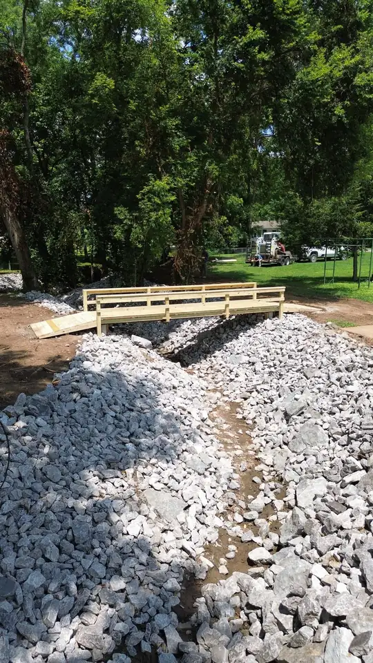 Aerial drone view — riprap drainage channel and pressure-treated bridge, Nashville TN