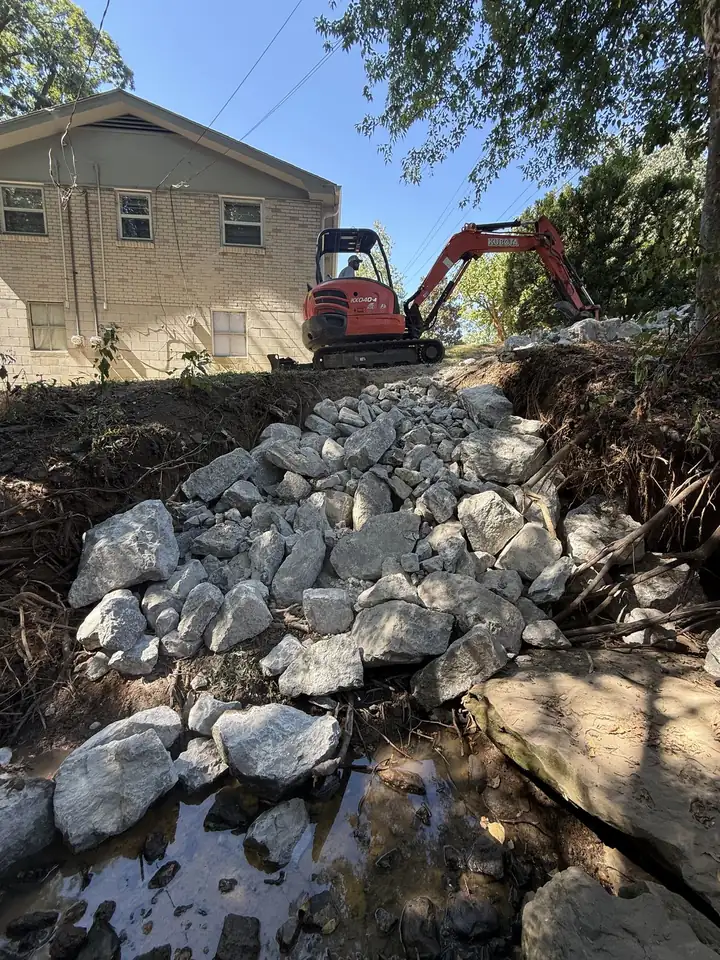 Kubota mini excavator setting Class B riprap on an eroded creek bank — Nashville TN